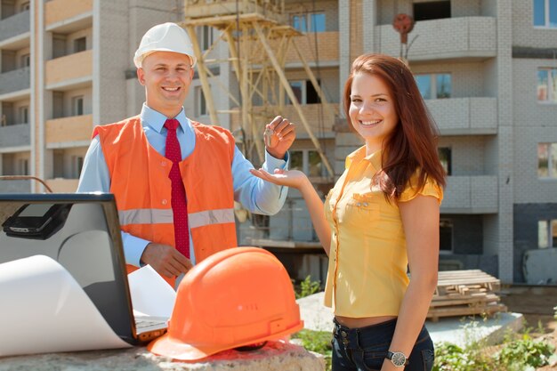 Representative of a restoration company with orange vest and hard hat meeting woman in front of construction site.